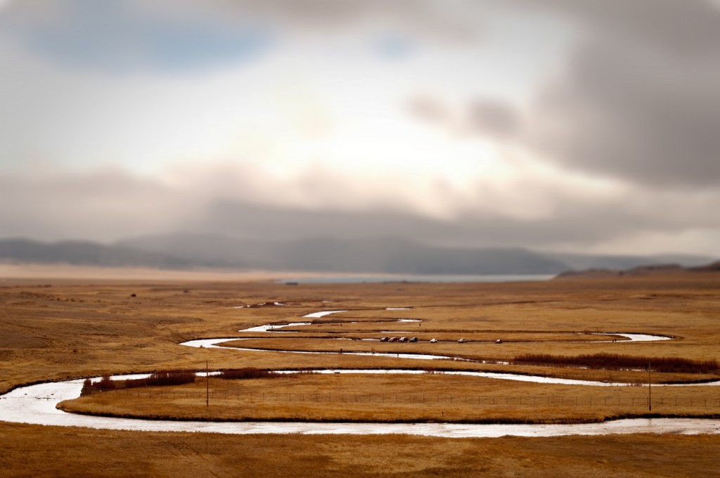 A river runs through a brown field with mountains in the background.