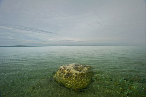 A rock sits in the middle of a body of water.