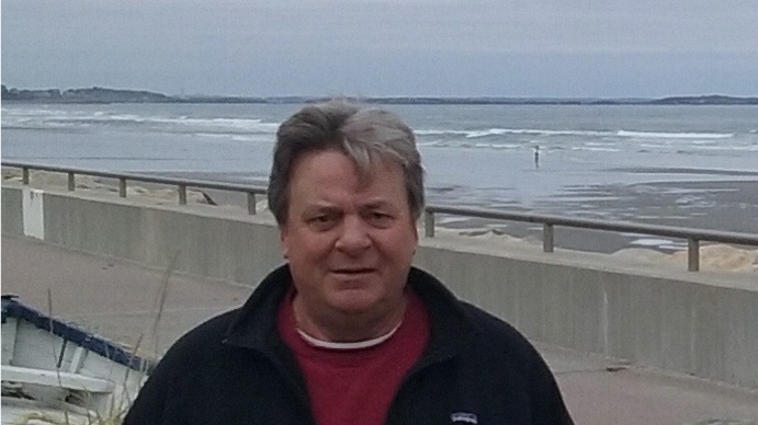 A man in a red jacket standing next to the ocean.