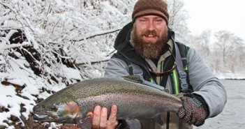 A bearded man holding a rainbow trout in the snow.
