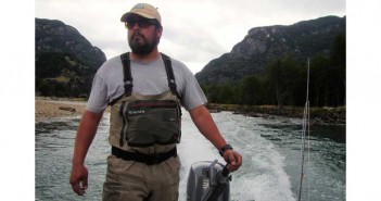 A man standing on a boat in front of mountains.