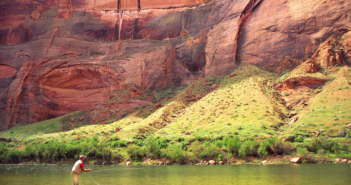 A man is fishing in a river near a rock formation.