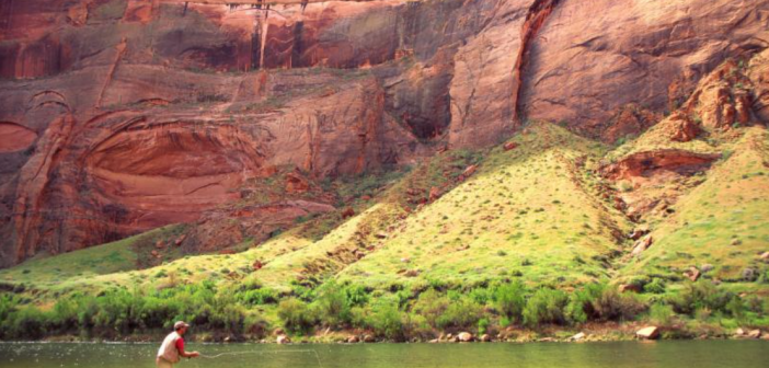 A man is fishing in a river near a rock formation.