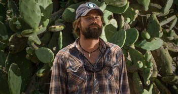 A bearded man standing in front of a cactus.
