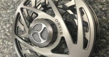 A grey fly reel with a metal handle.