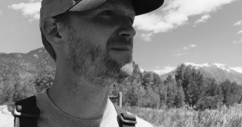 A black and white photo of a man in a hat standing in a field.