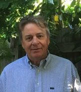 A man in a blue shirt standing in front of a tree.