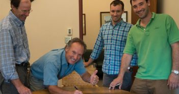 Four men standing around a table signing a document.