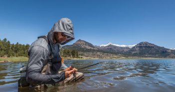 A man in a hoodie holding a fly rod in the water.