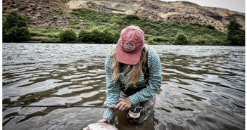 A woman in a red hat is holding a fly in the water.
