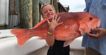 A young girl holding a large red snapper on a boat.
