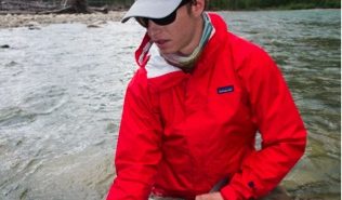 A man in a red jacket holding a fish in a river.