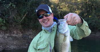A man holding up a large bass on a river.