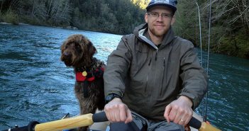 A man and a dog in a boat on a river.