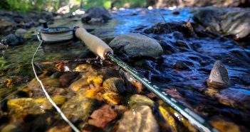 A fly fishing rod resting on rocks in a stream.