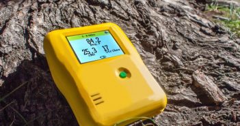 A yellow thermometer sitting on top of a tree stump.