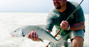 A man holding a striped bass in shallow water.