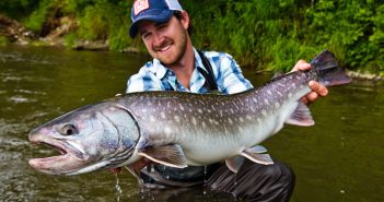 A man holding up a large fish in a river.