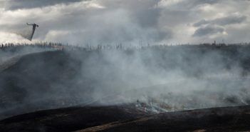 A firefighter flies over a hill with smoke coming from it.
