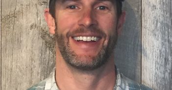 A smiling man wearing a plaid shirt and hat.