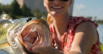 A woman holding a large bass in her hand.
