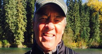 A man smiles while holding a fly rod in front of a river.