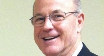 A man wearing glasses and a suit is smiling.