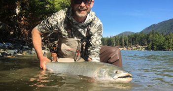 A man holding a large salmon in the water.