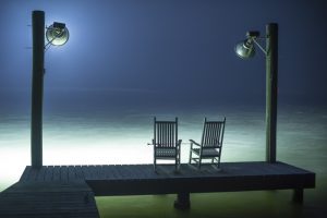 Two rocking chairs on a dock at night.