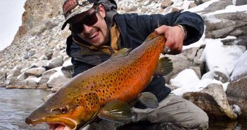 A man holding up a brown trout in the snow.