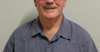A man with glasses and a moustache standing in front of a wall.