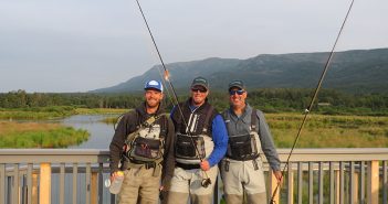 Three men standing on a bridge with fishing rods.