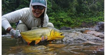 A woman holding a yellow fish in a river.