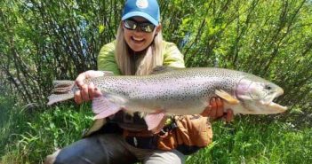 A woman holding up a rainbow trout.