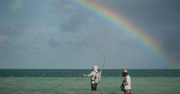 Two men fishing in the ocean under a rainbow.