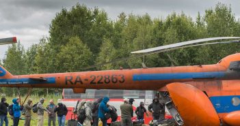 A group of people standing around an orange helicopter.