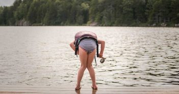 A girl in a bikini standing on a dock next to a lake.