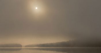 The sun rises over a foggy lake.