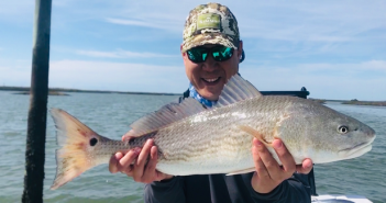 A man holding up a redfish on a boat.