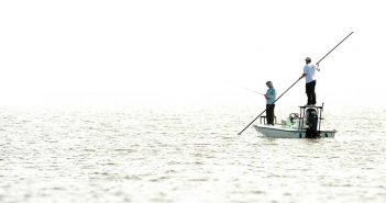 Two men fishing on a boat in the water.