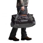 A man in camouflage carrying a duffel bag.