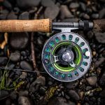 A fly rod and reel laying on rocks.