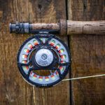 A fly fishing reel hanging on a wooden wall.