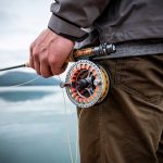 A man holding a fly fishing reel on a lake.