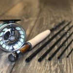 A fly rod and reel sitting on a wooden table.