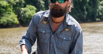 A bearded man holding a fishing rod in a river.