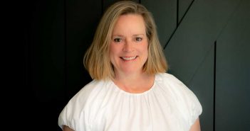 A woman in a white shirt smiling in front of a black wall.