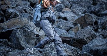 A man is standing on a rocky area with a fly rod.