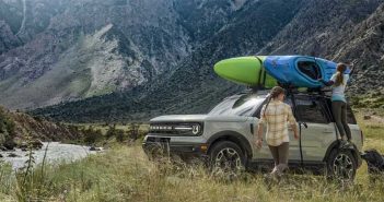The 2020 ford bronco is parked next to a river with a kayak on top.