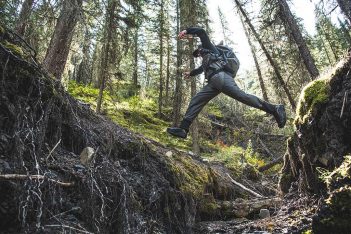 A man jumping over a stream in the woods.